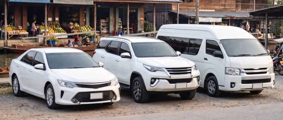 A white sedan, SUV and van parked by a canal-side fruit market